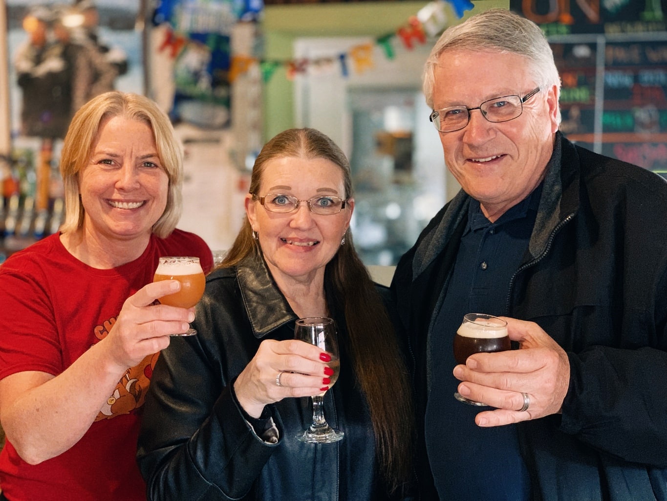 three people smiling and lifting beer glasses